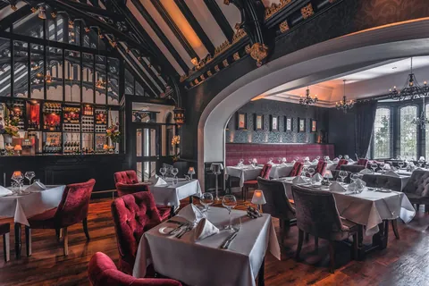 The dining room beneath its timbered ceiling, with the stone archway and wine bar beyond