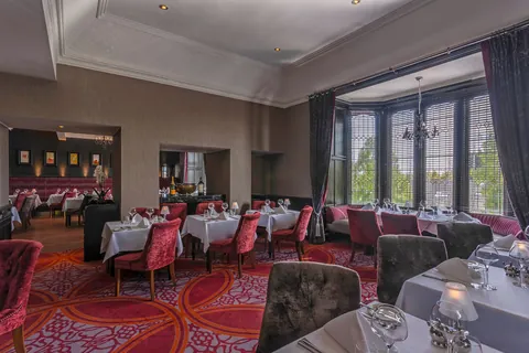 The dining room bay window, with crimson chairs and tables laid for dinner