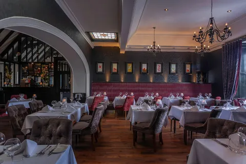 Tables set with white linen along the crimson banquette wall and framed artwork