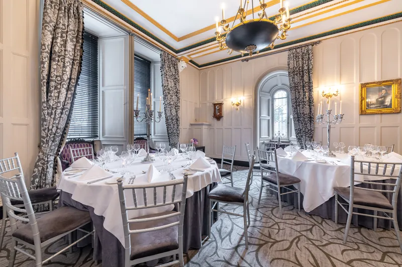 The Tower Suite private dining room: two round tables laid for dinner beneath a gilded ceiling and brass chandelier, with patterned drapes and panelled walls