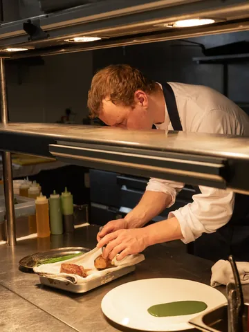 A chef finishing a plate at the pass under the heat lamps