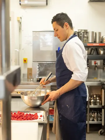 A chef whisking a sauce, with fresh raspberries ready on the counter